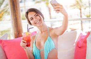 Young pretty woman taking a selfie with mobile smart phone in a beach club